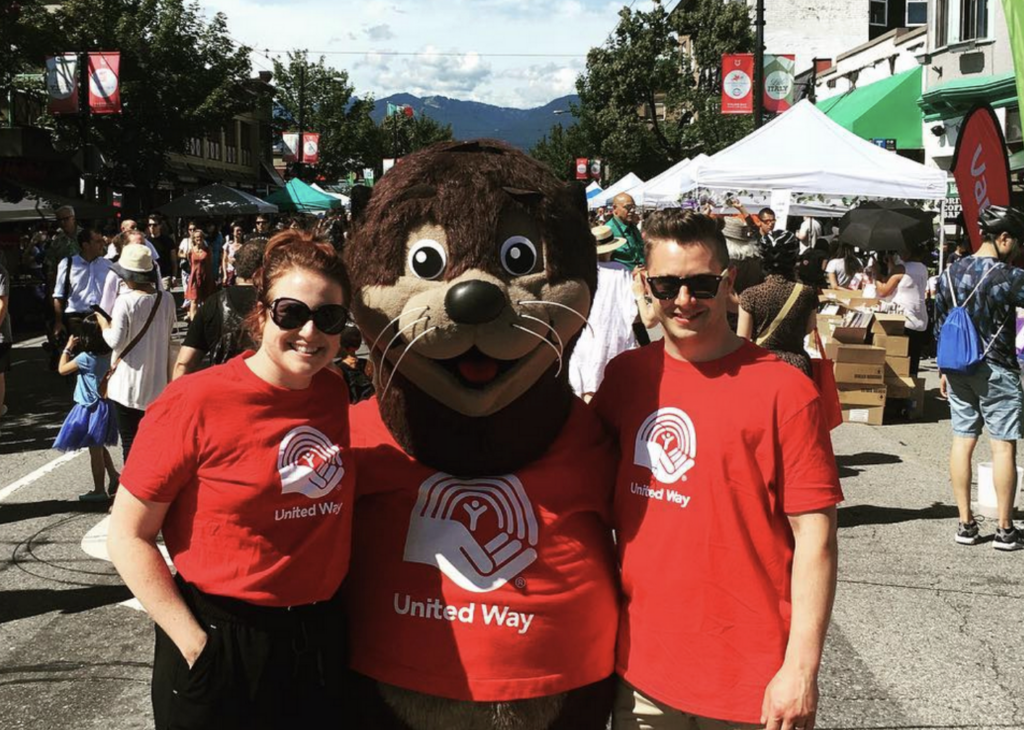 a woman and a man in red shirts stand next to a sea otter mascot 